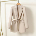 Blazer beige élégant pour femme avec ceinture, suspendu sur un cintre en bois. Mode féminine, veste chic, tenue professionnelle.