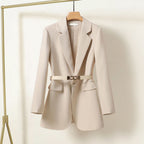 Blazer beige élégant pour femme avec ceinture, suspendu sur un cintre en bois. Mode féminine, veste chic, tenue professionnelle.