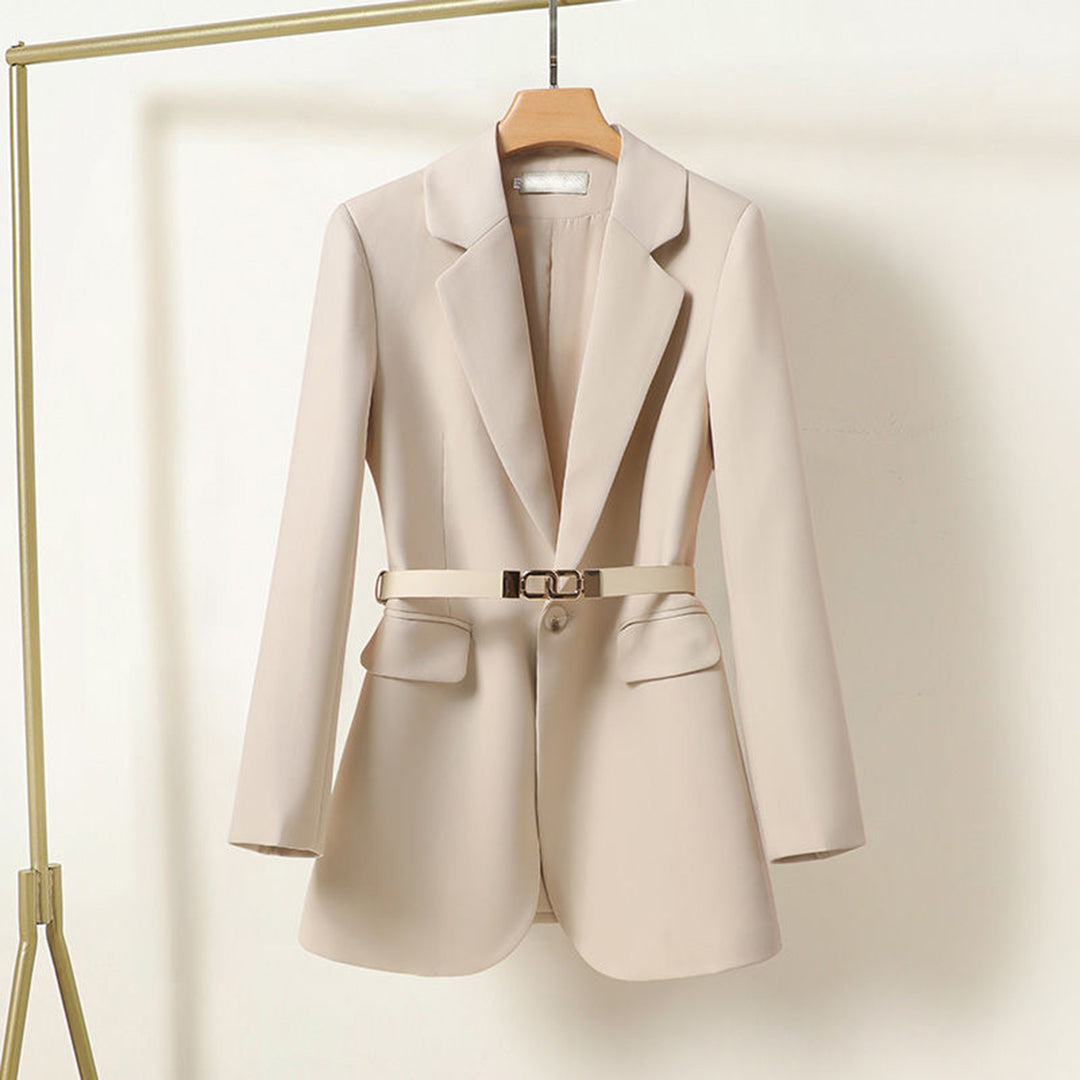 Blazer beige élégant pour femme avec ceinture, suspendu sur un cintre en bois. Mode féminine, veste chic, tenue professionnelle.