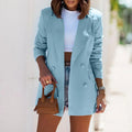 Femme en blazer bleu clair, t-shirt blanc et short en jean, tenant un sac à main marron. Mode estivale élégante et décontractée.