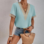 Femme en blouse bleu clair avec dentelle, short en jean, portant un sac en osier. Mode estivale, tenue décontractée, accessoires dorés.