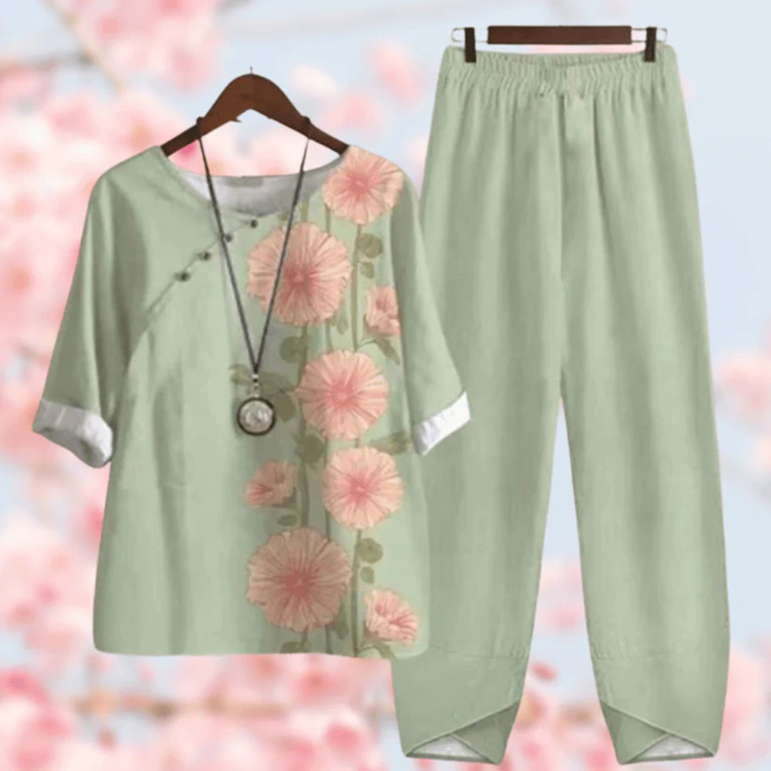 Tenue en lin vert clair avec motifs floraux roses, comprenant un haut à manches trois-quarts et un pantalon ample. Fond flou de fleurs de cerisier.