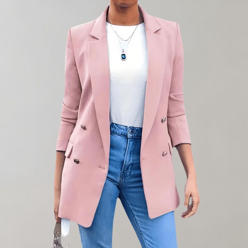 Femme portant un blazer rose élégant, t-shirt blanc et jean bleu, accessoirisée d'un collier pendentif. Mode féminine chic et moderne.