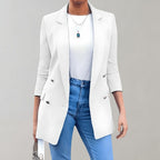 Femme portant un blazer blanc élégant, chemise blanche et jean bleu, accessoirisée d'un collier pendentif et d'un sac à main, sur fond gris.