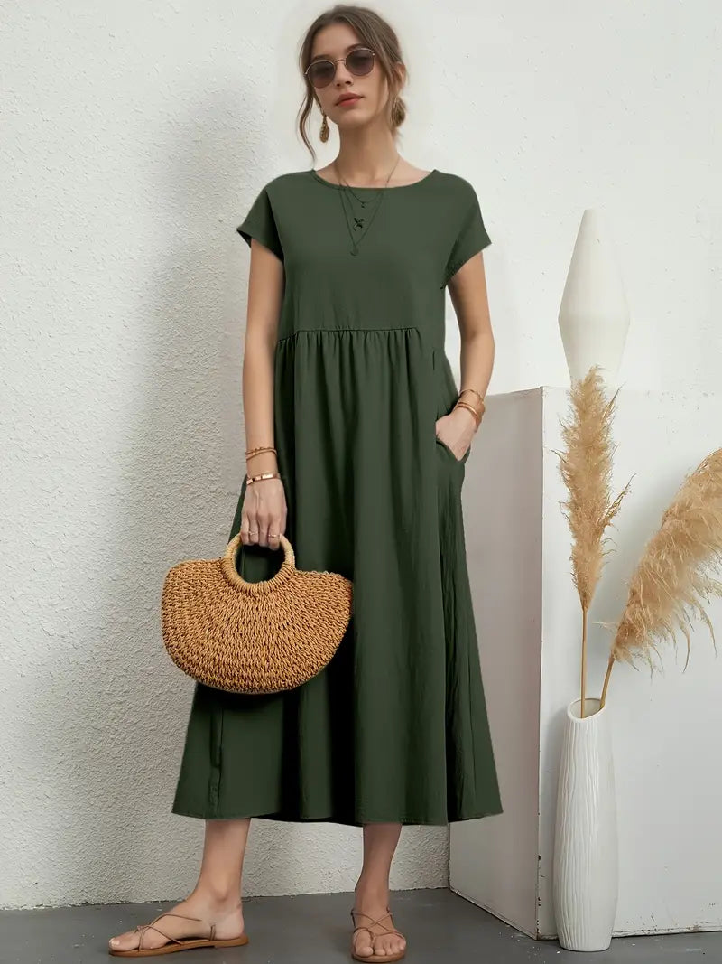 Robe longue verte femme, manches courtes, avec sac en osier, lunettes de soleil, sandales beiges, décor minimaliste, vase pampas.