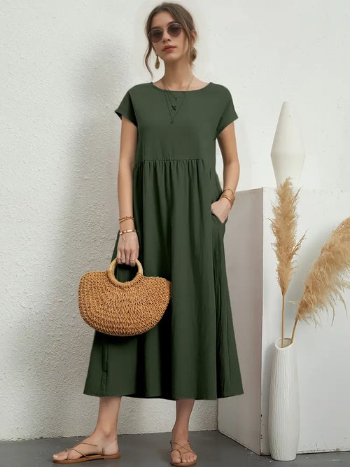 Robe longue verte femme, manches courtes, avec sac en osier, lunettes de soleil, sandales beiges, décor minimaliste, vase pampas.