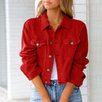Femme portant une veste en jean rouge, manches retroussées, sur un t-shirt blanc, avec un collier doré, devant un mur blanc. Mode décontractée tendance.