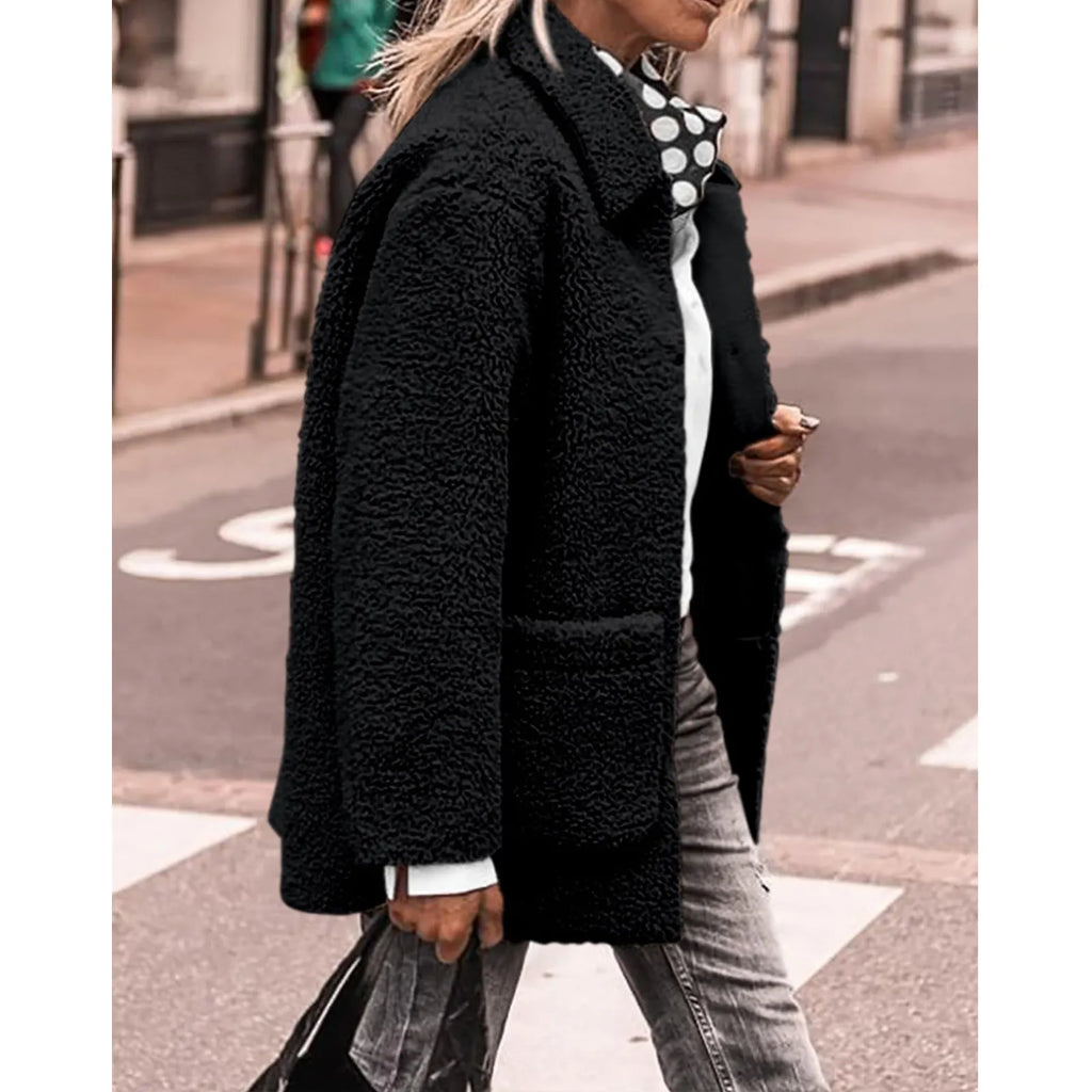 Femme portant un manteau en fausse fourrure noir, chemise blanche, foulard à pois, jeans gris, marchant en ville. Mode automne-hiver tendance.