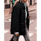 Femme portant un manteau en fausse fourrure noir, chemise blanche, foulard à pois, jeans gris, marchant en ville. Mode automne-hiver tendance.