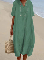 Robe verte ample en lin sur plage, femme tenant un sac en osier. Mode estivale, tenue décontractée, style plage chic.