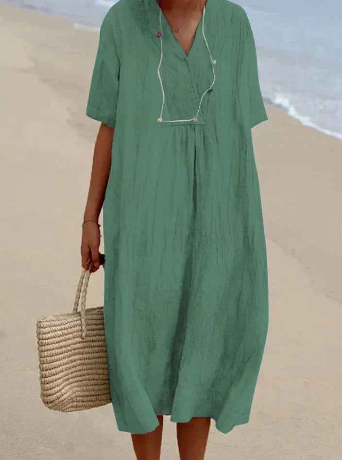 Robe verte ample en lin sur plage, femme tenant un sac en osier. Mode estivale, tenue décontractée, style plage chic.