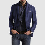Homme portant une veste bleue élégante, chemise à motifs, jean décontracté et montre-bracelet. Mode masculine chic et moderne.