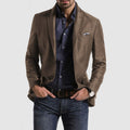 Homme portant une veste marron élégante, chemise bleue à motifs, jean décontracté, montre-bracelet et pochette assortie. Mode masculine chic.