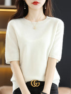Femme portant un pull blanc en cachemire, collier délicat et ceinture noire avec boucle dorée. Mode élégante et tendance automne-hiver.