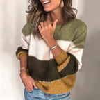 Femme souriante portant un pull tricolore à rayures vert, blanc et jaune moutarde, manches longues, avec jeans. Mode automne-hiver tendance.