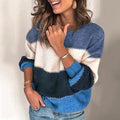 Femme souriante portant un pull tricolore bleu, blanc et beige, manches retroussées, avec des bracelets dorés, posant devant un fond neutre.
