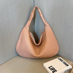 Sac à main en cuir tressé rose posé sur un canapé gris, à côté d'un livre intitulé "Love Your Life". Accessoire mode élégant et tendance.