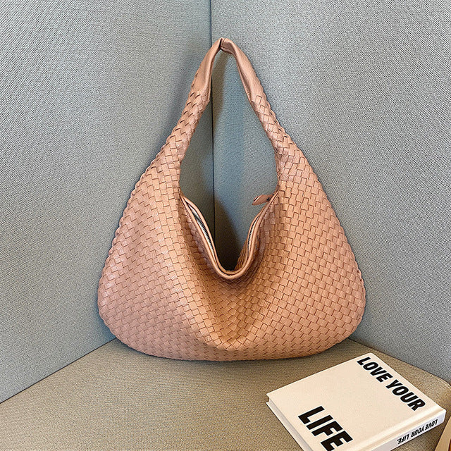 Sac à main en cuir tressé rose posé sur un canapé gris, à côté d'un livre intitulé "Love Your Life". Accessoire mode élégant et tendance.