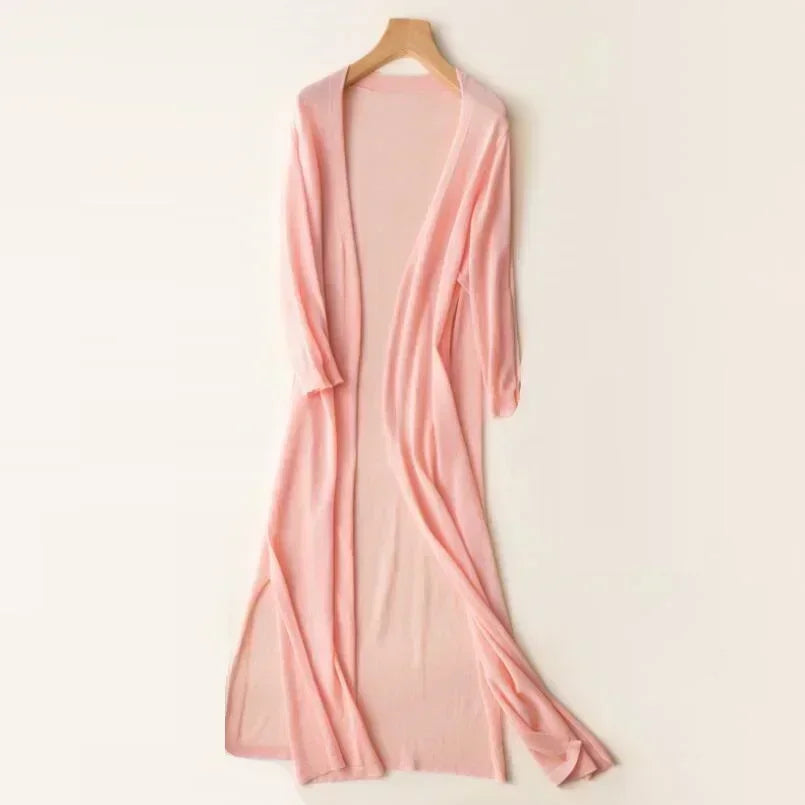 Robe longue rose pâle en maille, suspendue sur un cintre en bois, style élégant et décontracté, idéale pour l'été et les soirées décontractées.
