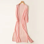 Robe longue rose pâle en maille, suspendue sur un cintre en bois, style élégant et décontracté, idéale pour l'été et les soirées décontractées.