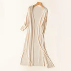 Gilet long beige en tricot, manches longues, ouvert, suspendu sur un cintre en bois. Mode automne, vêtement confortable et élégant.