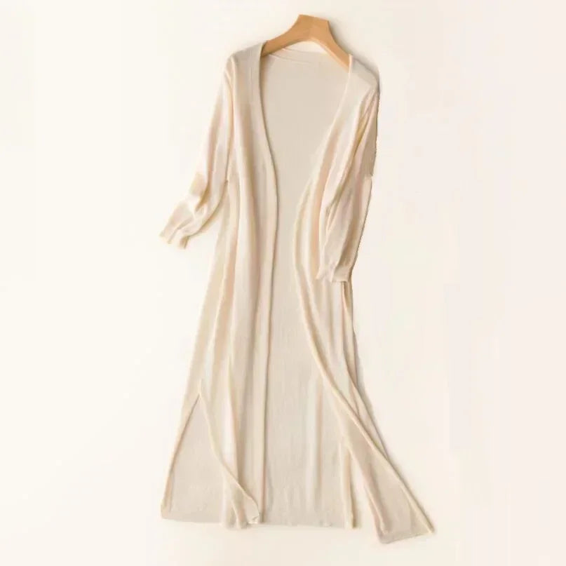Gilet long beige en tricot, manches longues, ouvert, suspendu sur un cintre en bois. Mode automne, vêtement confortable et élégant.