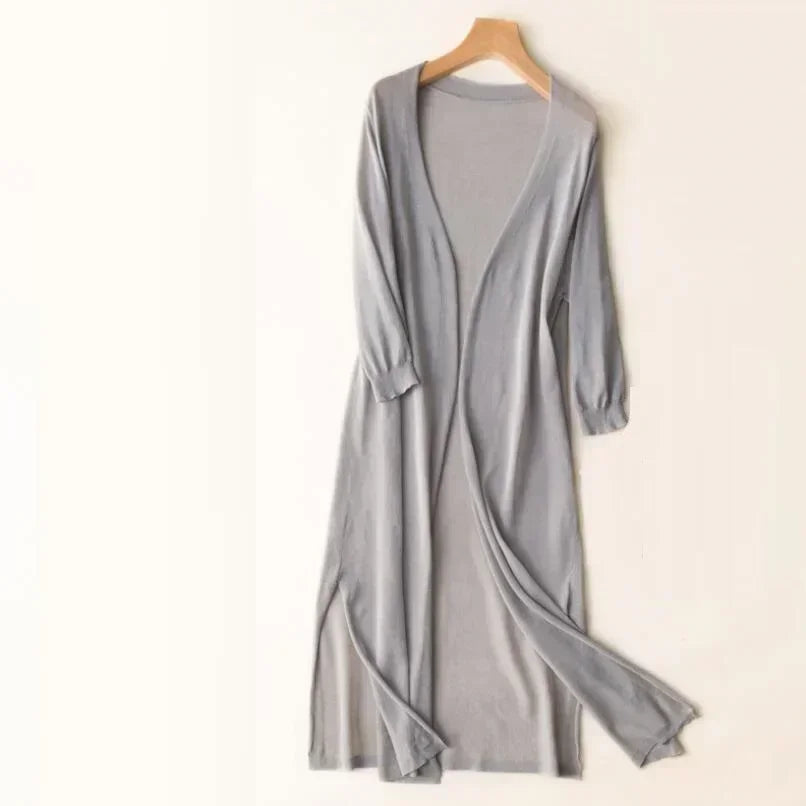 Cardigan long gris en tricot léger, manches longues, ouvert sur le devant, suspendu sur un cintre en bois. Mode féminine élégante et confortable.