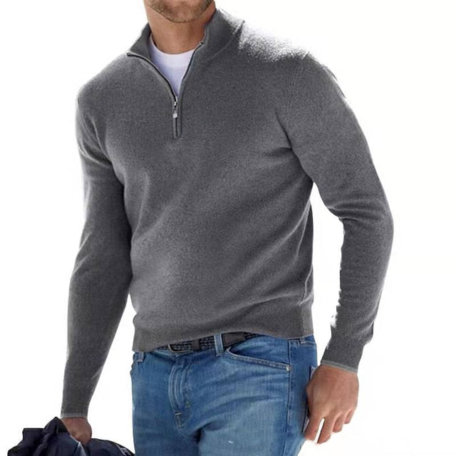 Homme portant un pull gris à col zippé, style décontracté, avec un jean bleu. Mode masculine élégante et moderne.