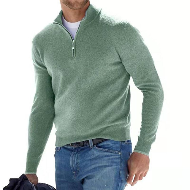 Homme portant un pull vert à col zippé, style décontracté, avec un jean bleu. Mode masculine, tenue automne-hiver, look moderne et élégant.