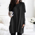 Femme portant une robe pull noire ample, tenant une tasse à motifs. Mode décontractée, style automne-hiver, confort et élégance.