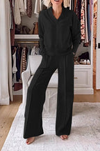 Femme en ensemble noir confortable, debout pieds nus dans un dressing moderne avec vêtements suspendus et étagères blanches en arrière-plan.