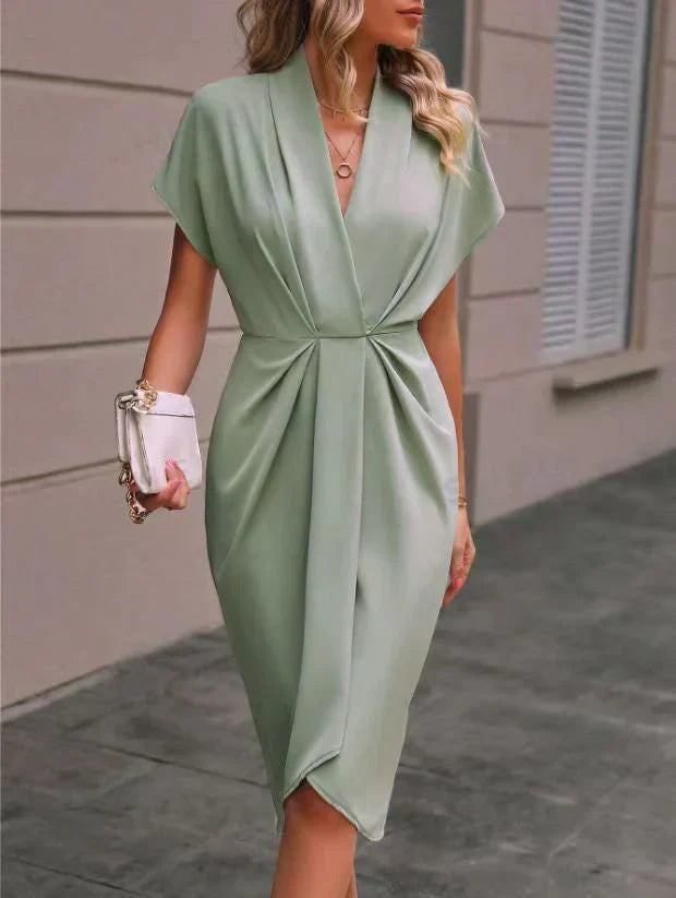 Robe verte élégante drapée, manches courtes, portée par une femme avec sac à main blanc. Mode féminine chic, tenue de soirée tendance.