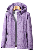 Veste imperméable violette à motifs floraux, capuche ajustable, fermetures éclair noires, accrochée sur un cintre en bois, idéale pour la randonnée.