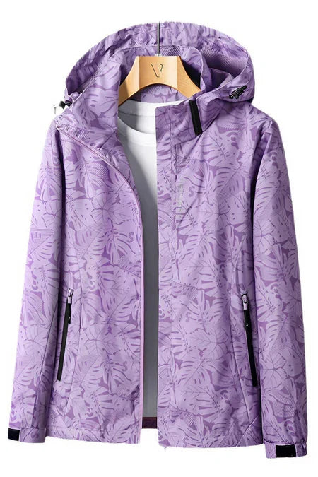 Veste imperméable violette à motifs floraux, capuche ajustable, fermetures éclair noires, accrochée sur un cintre en bois, idéale pour la randonnée.