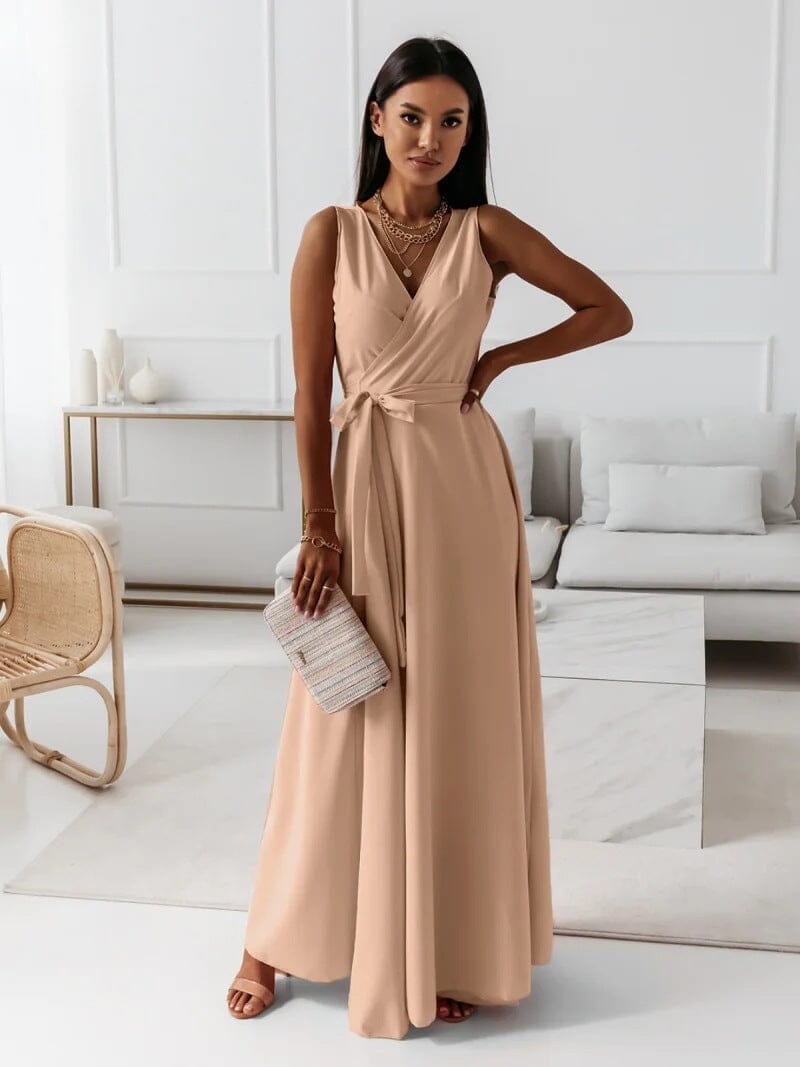 Femme portant une robe longue beige élégante, tenant un sac à main texturé, posant dans un salon moderne. Mode féminine, tenue chic, style contemporain.