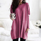 Femme portant une tunique rose ample, tenant une tasse à motifs, dans un intérieur lumineux. Mode décontractée, style automne-hiver, confort.