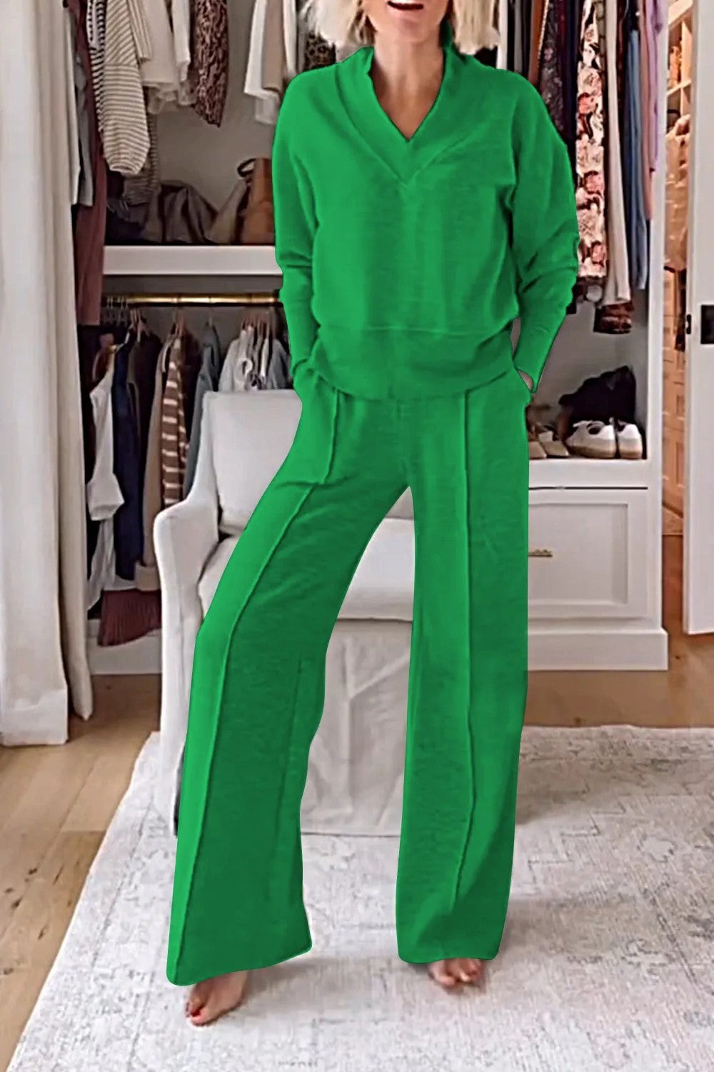 Femme portant un ensemble vert confortable dans un dressing moderne, avec des vêtements suspendus et un fauteuil blanc. Mode décontractée élégante.