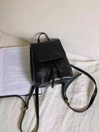 Sac à dos en cuir noir élégant posé sur un lit blanc, à côté d'une feuille de papier imprimée. Accessoire mode tendance et pratique.
