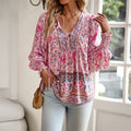 Femme portant un chemisier bohème rose à motifs floraux, manches longues, avec un sac en osier, posant près d'une fenêtre lumineuse.