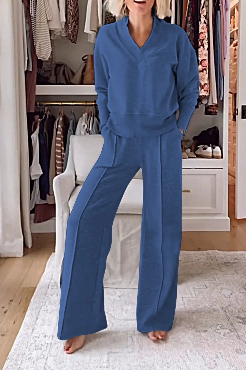 Femme portant un ensemble bleu confortable dans un dressing moderne, avec des vêtements suspendus et un fauteuil blanc. Mode décontractée élégante.