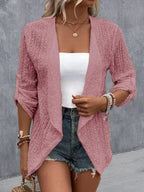 Femme portant un cardigan rose en dentelle, débardeur blanc, short en jean, accessoires en perles, style décontracté chic, mode estivale tendance.