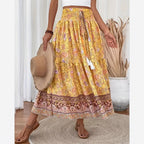 Jupe longue bohème jaune à motifs floraux, ceinture élastique, tenue estivale décontractée, femme tenant un chapeau de paille, sandales marron.