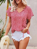 Femme en blouse rouge à motifs floraux, short blanc déchiré, tenant un chapeau de paille. Mode estivale, tenue décontractée, style plage.