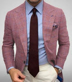 Homme en costume rose élégant, chemise bleue, cravate bordeaux, pantalon blanc. Mode masculine, tenue professionnelle chic.