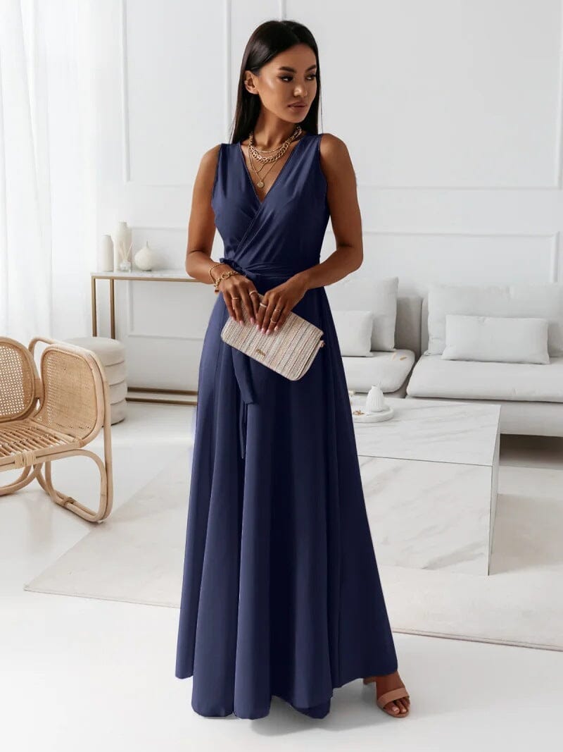 Femme élégante en robe longue bleue, tenant une pochette beige, debout dans un salon moderne. Mode féminine, style chic, tenue de soirée.