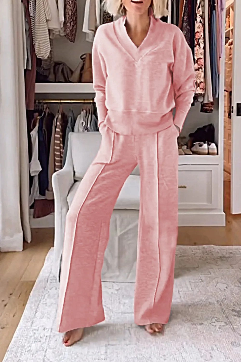 Femme portant un ensemble rose confortable dans un dressing moderne, avec un pull et un pantalon ample. Mode décontractée, tenue élégante à la maison.