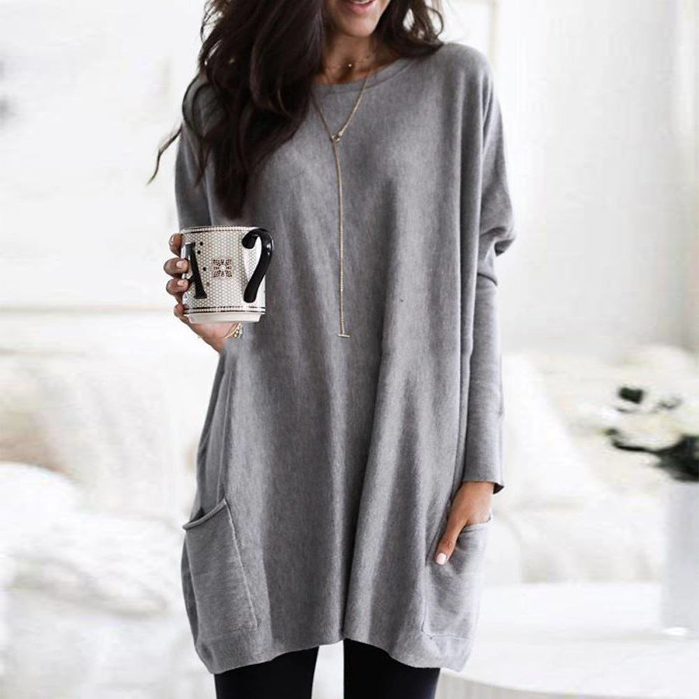 Femme portant une robe pull grise ample, tenant une tasse à motifs, dans un intérieur lumineux. Mode décontractée, style automne-hiver.