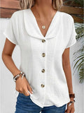 Femme portant un chemisier blanc en coton à boutons, manches courtes, col large, avec un collier doré et des bracelets, style décontracté chic.