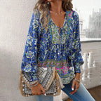 Femme portant une blouse bohème bleue à motifs floraux, tenant un sac à main ethnique avec franges et perles, sur fond de balcon urbain.