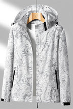 Veste imperméable à capuche pour femme, motif tropical blanc et gris, fermeture éclair, poches zippées, idéale pour randonnée et activités extérieures.